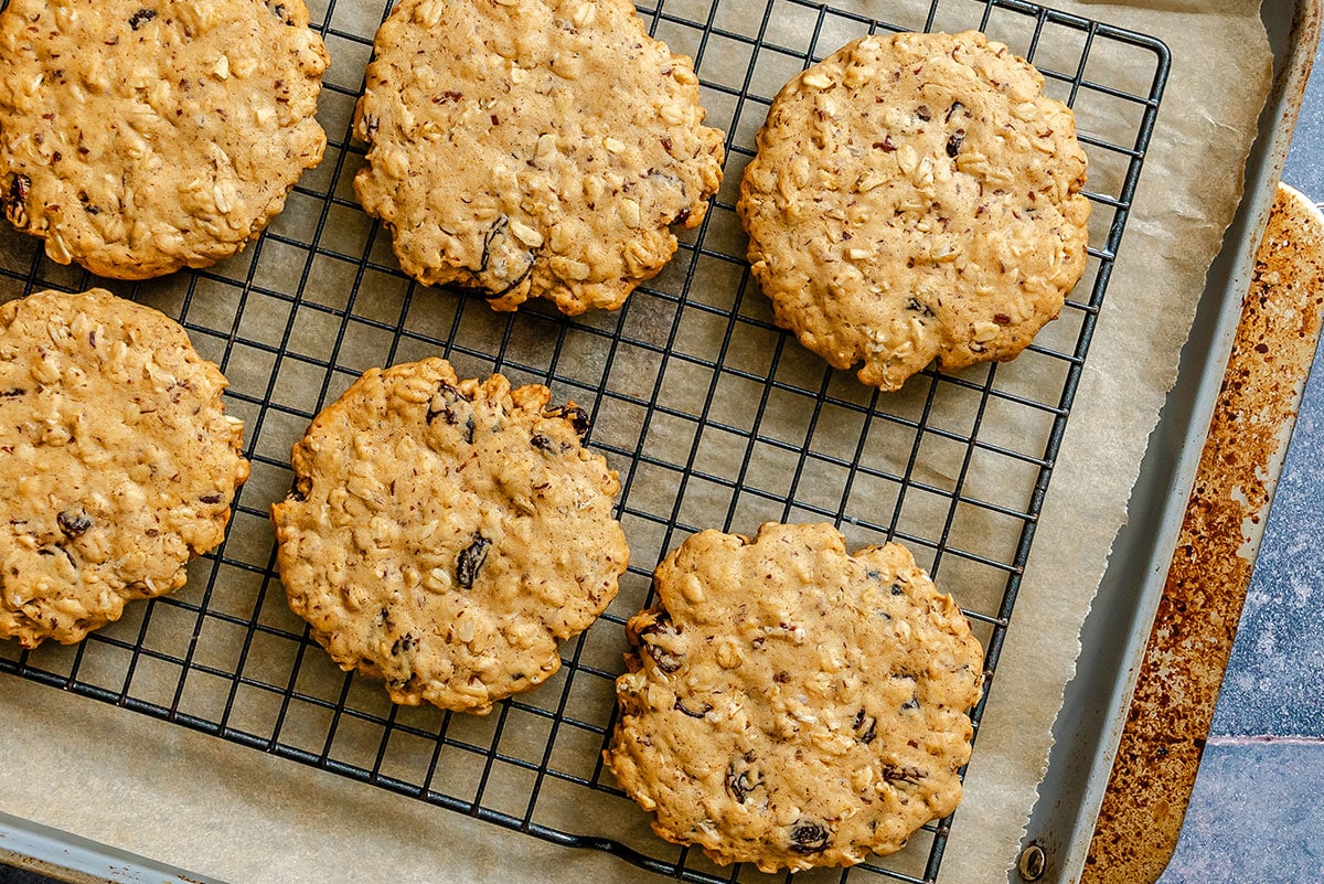 Six oatmeal cookies with raisins cooling on a black wire rack placed on a baking sheet lined with parchment paper.