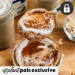 A spoonful of yogurt topped with cinnamon held above a jar, surrounded by jars and oats on a wooden surface. Plant pals exclusive and a lock icon are displayed. Perfect for pairing with ice cubes in your favorite holiday mocktail.