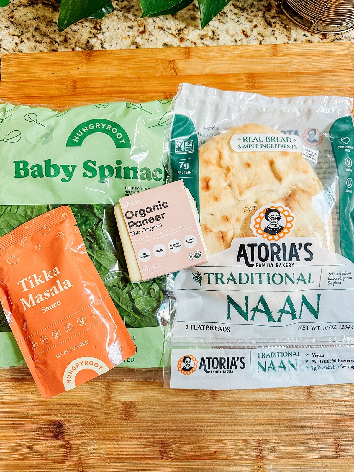 A package of baby spinach, a pouch of tikka masala sauce, organic paneer, and traditional naan on a wooden surfaceโperfect for easy vegetarian dinners or your next Hungryroot review.