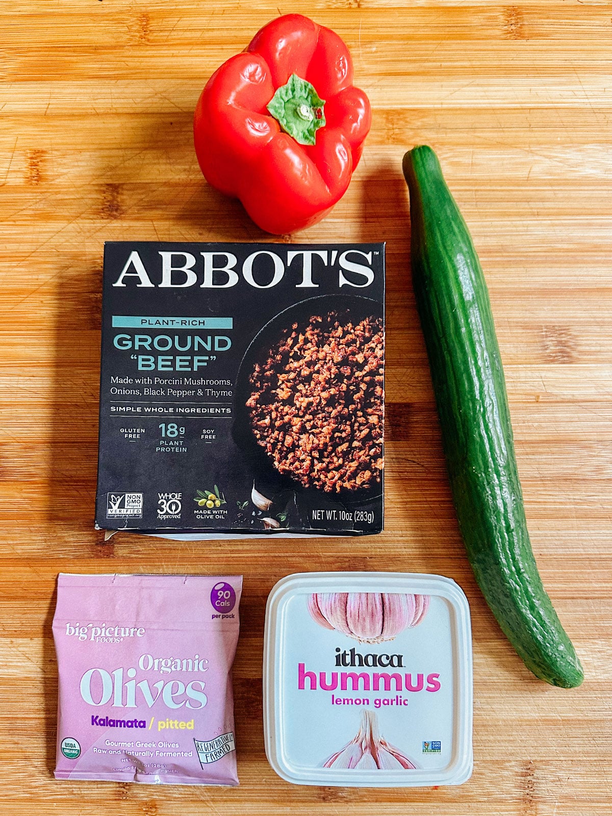 A red bell pepper, a box of plant-based ground beef, a cucumber, kalamata olives, and lemon garlic hummusโperfect ingredients for easy dinners or anyone seeking delicious vegetarian dinners.