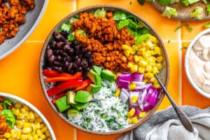 A bowl filled with black beans, seasoned ground meat, corn, red bell pepper, avocado, red onion, and cilantro rice, with a fork on the side.