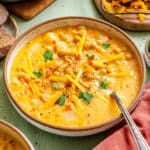 A bowl of creamy chickpea chowder soup topped with shredded cheddar cheese and parsley, with a spoon resting inside the bowl.