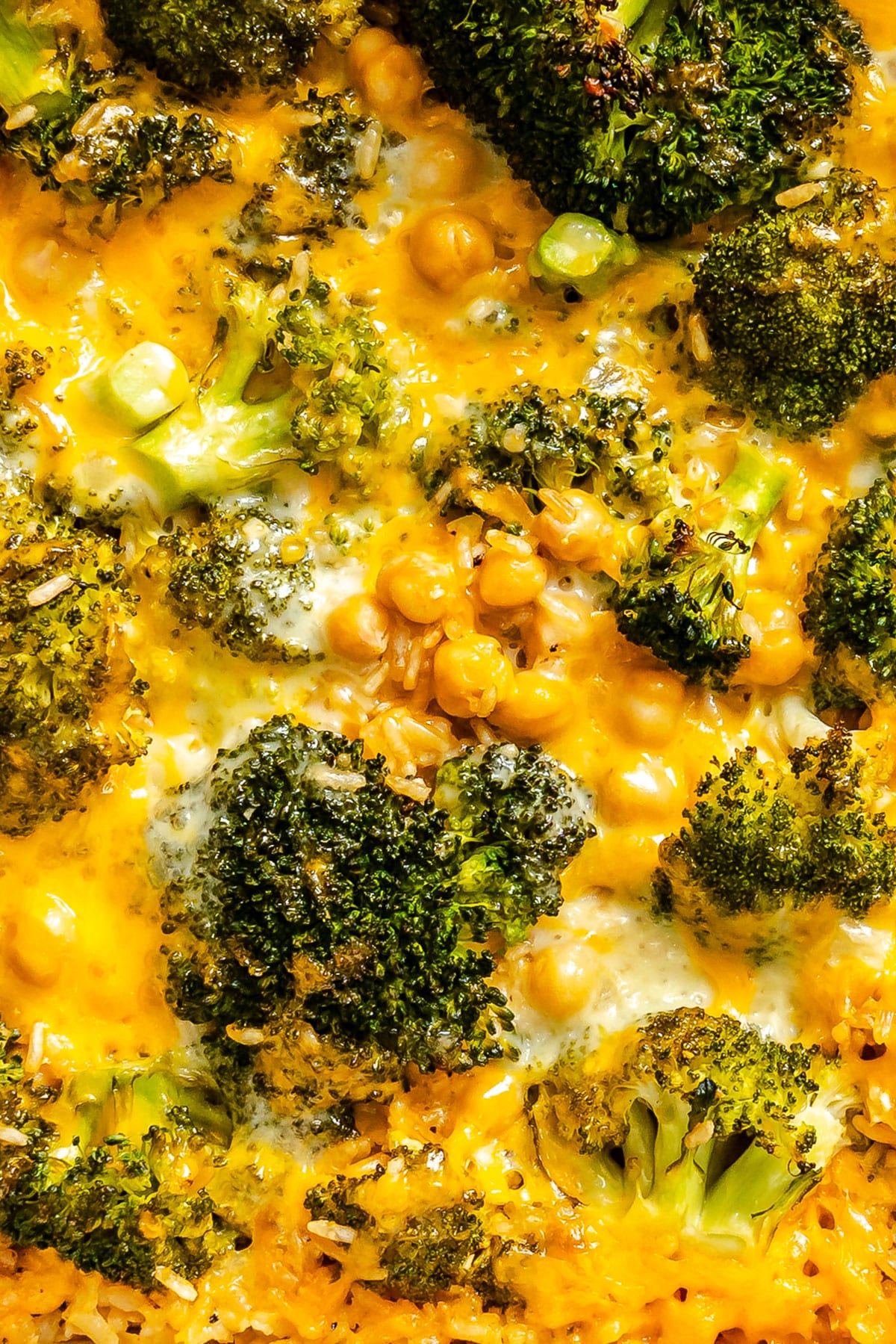 Close-up of baked broccoli and chickpeas covered in melted cheddar cheese and herbs.