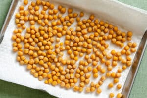 A baking sheet lined with paper towels holds a single layer of drained chickpeas spread out to dry.
