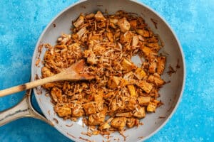 Cooked shredded jackfruit in a white skillet with a wooden spoon, set on a blue countertop.