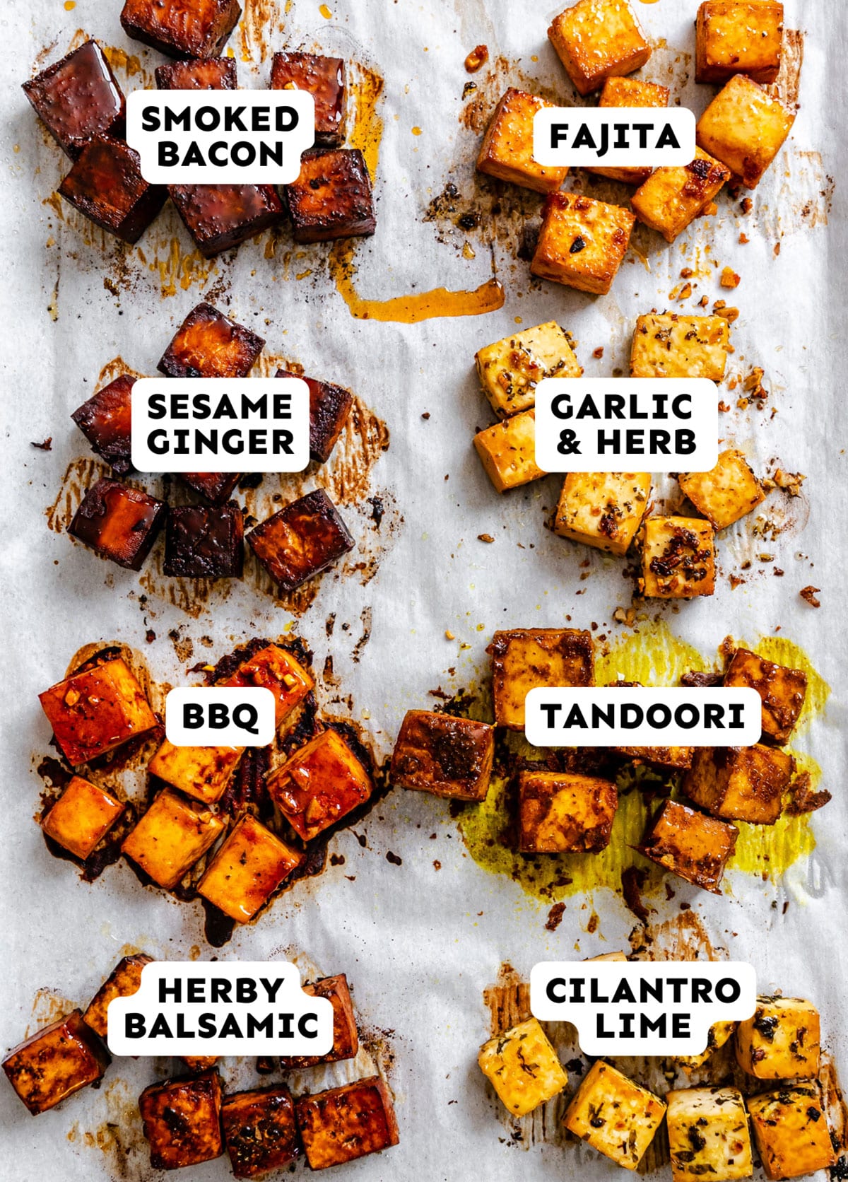 Nine groups of cubed tofu on parchment paper, each labeled with a different seasoning: smoked bacon, fajita, sesame ginger, garlic & herb, BBQ, tandoori, herby balsamic, and cilantro lime.
