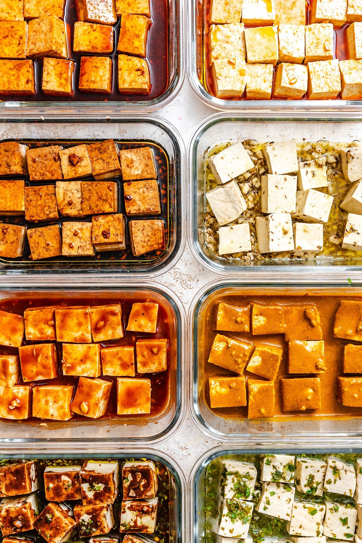 Eight glass containers filled with cubed tofu marinating in different sauces, arranged in a grid pattern.