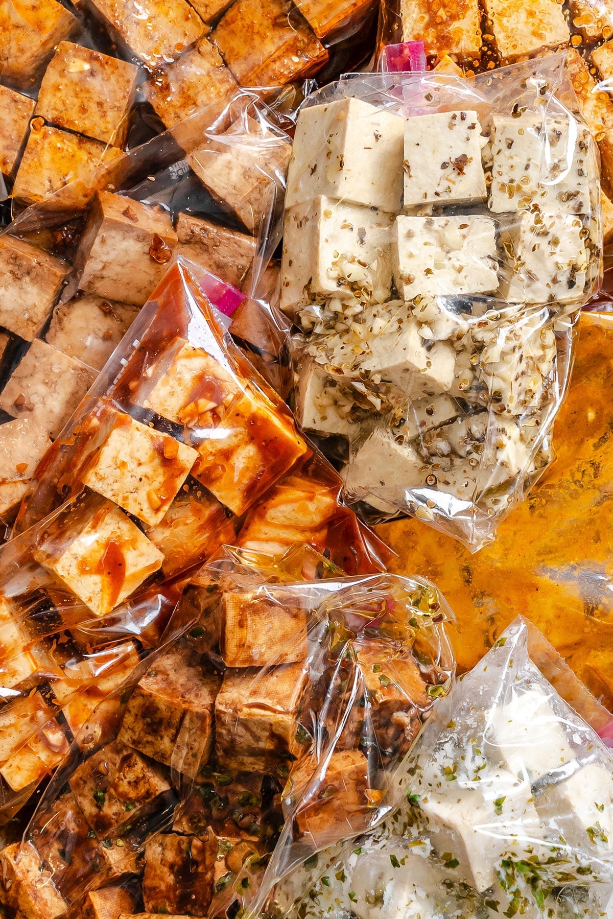 Cubes of tofu in clear plastic bags, marinated in various seasonings and sauces, displayed side by side.