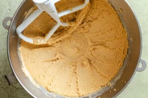 Banana bread dough being mixed in a metal stand mixer bowl with a paddle attachment.