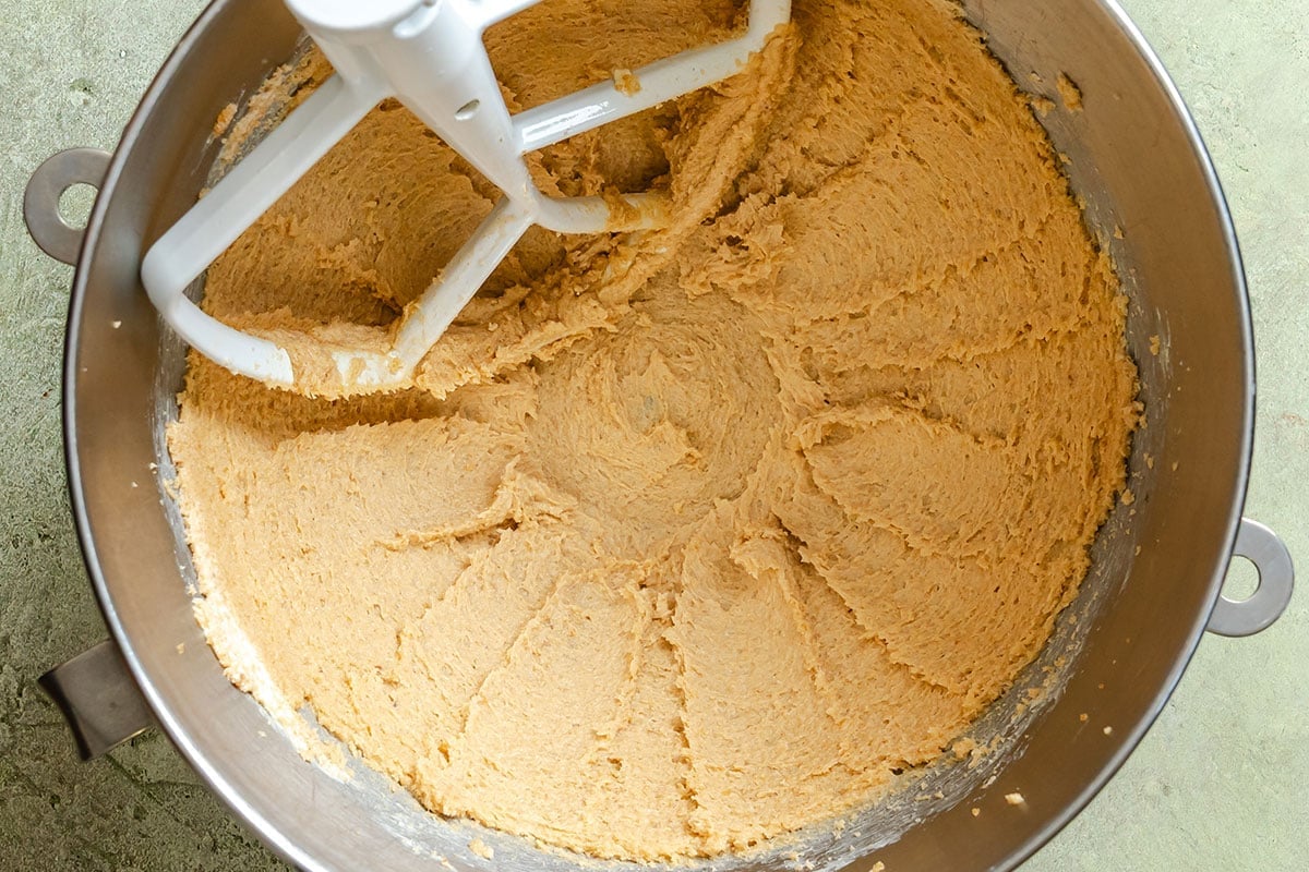 Banana bread dough being mixed in a metal stand mixer bowl with a paddle attachment.