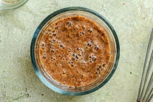 A glass bowl filled with a bubbly flaxseed and water mixture sits on a light-colored surface.