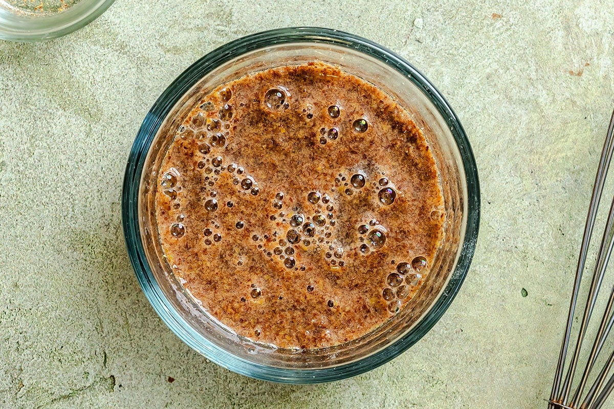 A glass bowl filled with a bubbly flaxseed and water mixture sits on a light-colored surface.