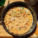 A skillet filled with creamy Marry Me Chickpeas stew, featuring tomatoes, herbs, and a light drizzle of cream, sits on a wooden surface in bright natural light—a high protein delight for any table.
