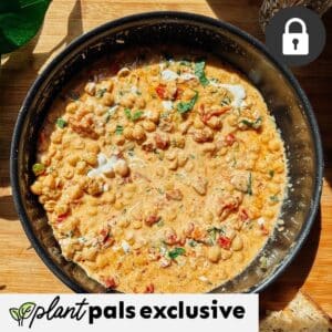 A pan of creamy Marry Me Chickpeas stew with tomatoes and herbs sits on a wooden surface. High Protein, plant pals exclusive, and a lock icon are overlaid in the corners.