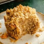 A partially eaten crumb-topped banana muffin sits on a plate, with crumbs scattered around it.