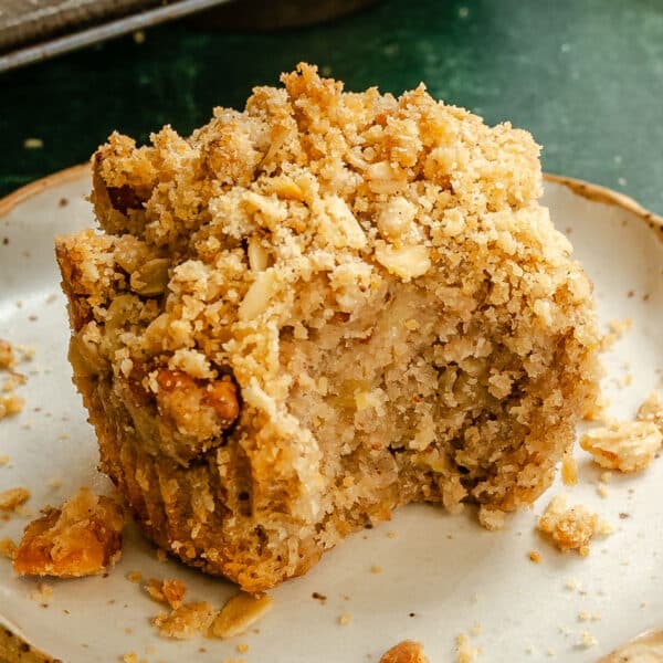 A partially eaten crumb-topped banana muffin sits on a plate, with crumbs scattered around it.