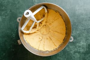 A metal mixing bowl filled with creamed cookie dough and a paddle attachment on a green countertop.