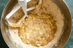 Mashed bananas and flour mixture in a metal mixing bowl with a stand mixer paddle attachment.
