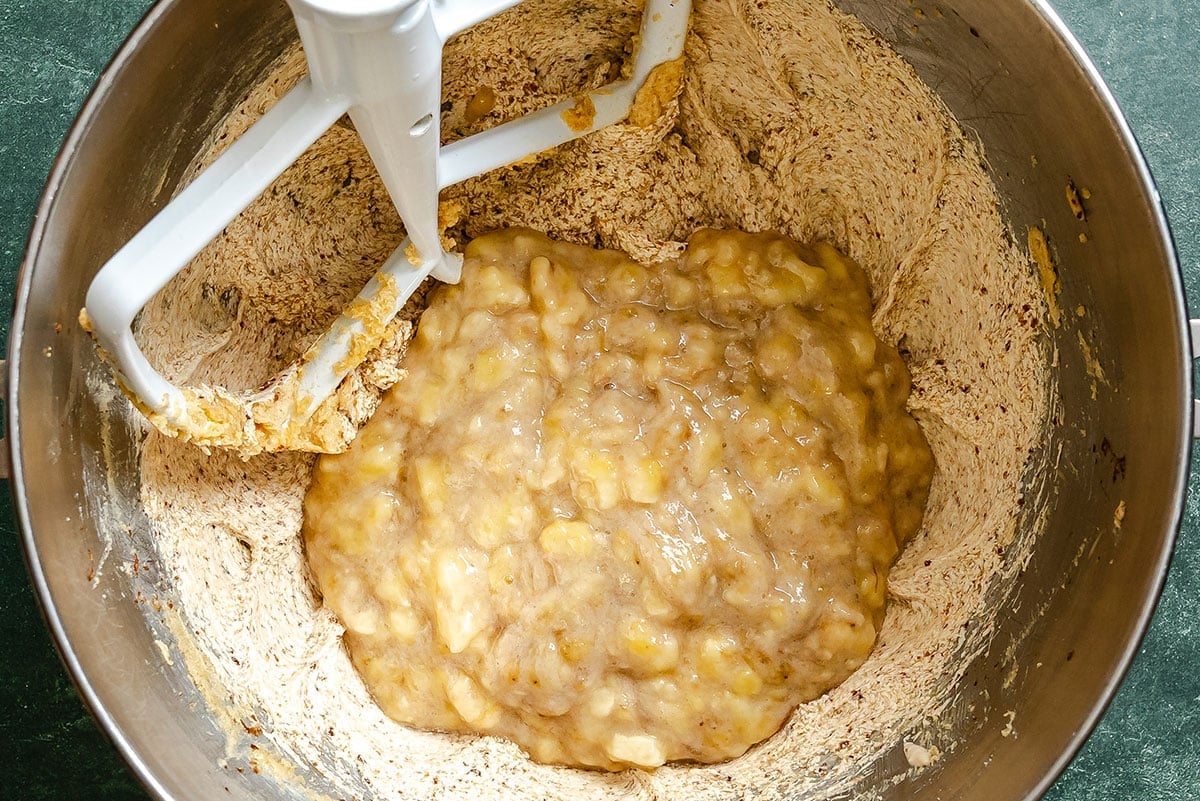 Mashed bananas and flour mixture in a metal mixing bowl with a stand mixer paddle attachment.