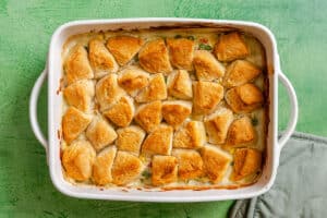 A delicious Vegetable Pot Pie casserole filled with creamy filling and topped with golden-brown biscuit pieces sits on a green surface next to a light-colored oven mitt.