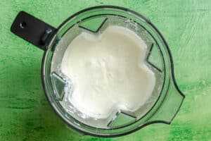 Overhead view of a blender containing a thick, white, creamy mixture—perfect as a base for a comforting vegetable pot pie or dump and bake casserole—set on a textured green surface.