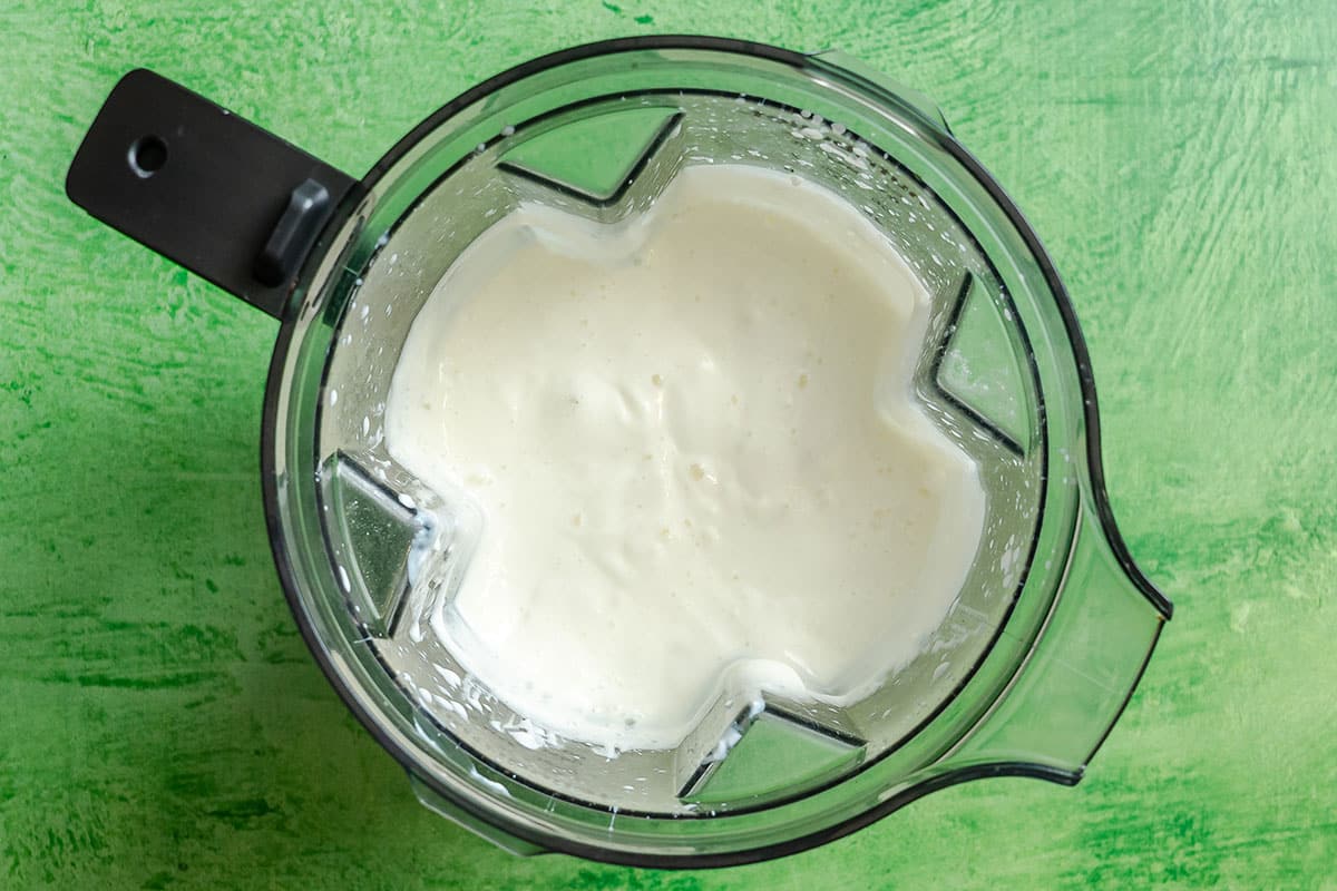 Overhead view of a blender containing a thick, white, creamy mixture—perfect as a base for a comforting vegetable pot pie or dump and bake casserole—set on a textured green surface.