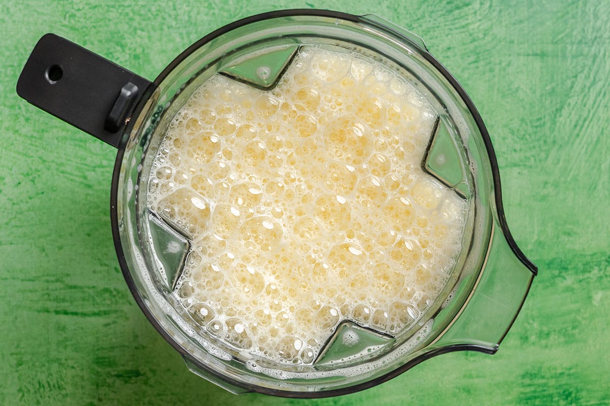 Top view of a blender containing a frothy, pale yellow liquid on a green surface.