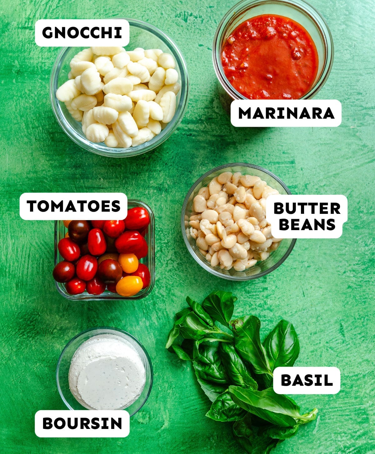Five labeled ingredients on a green surface: gnocchi, marinara sauce, tomatoes, butter beans, Boursin cheese, and fresh basil.