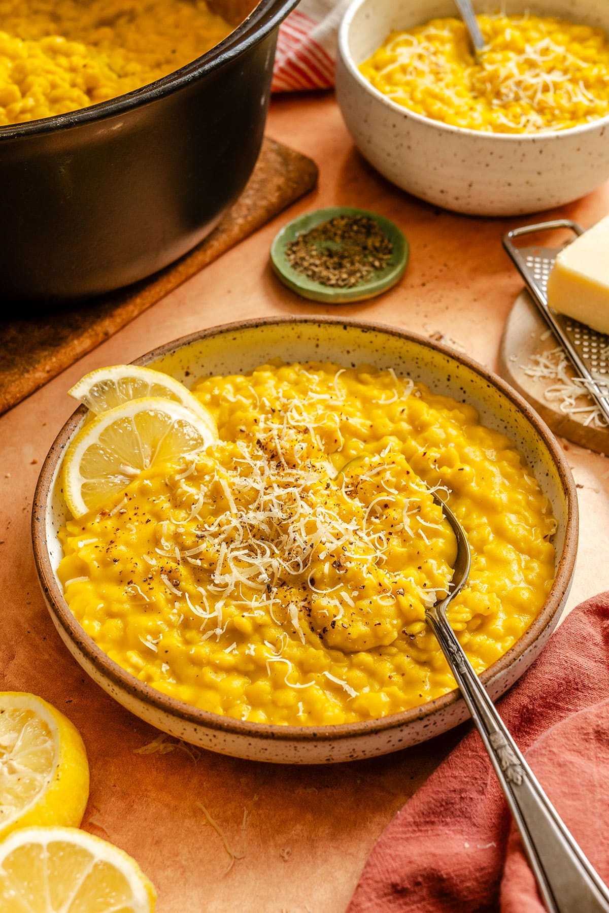A bowl of creamy lemon pepper Italian penicillin topped with grated cheese and black pepper, garnished with lemon slices, with a spoon resting in the bowl.