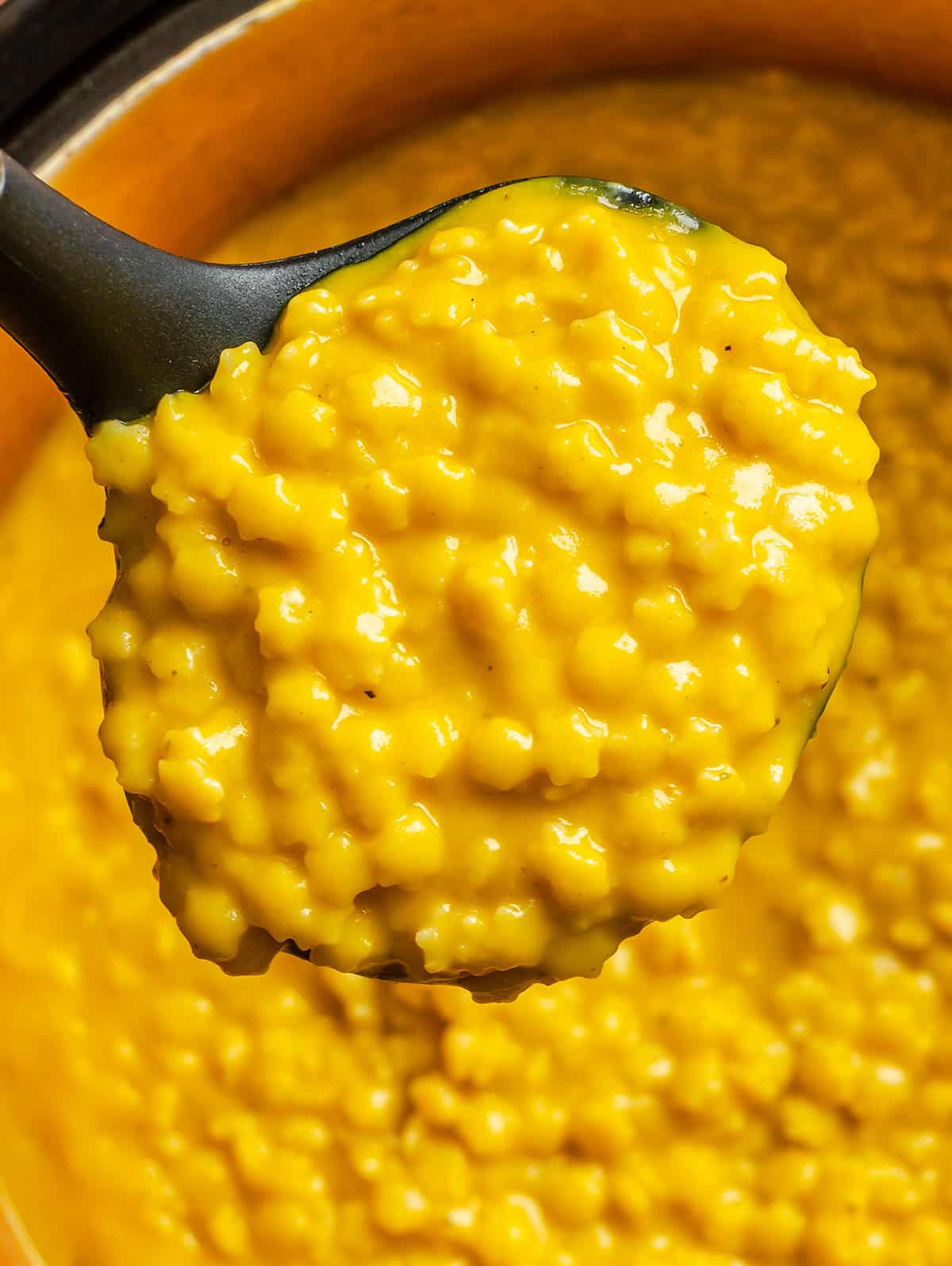 A close-up of a black ladle holding a serving of creamy yellow lemon pepper Italian penicillin, with more risotto visible in a pot below.