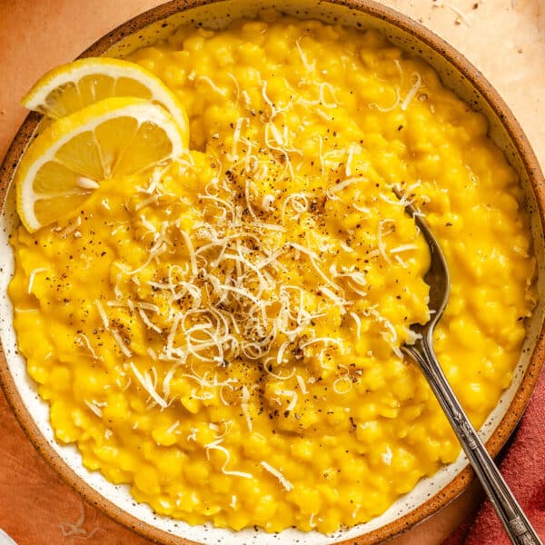 A bowl of lemon pepper Italian penicillin topped with grated cheese and black pepper, garnished with two lemon slices, with a spoon resting on the side.