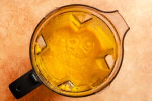 Top view of a blender containing a smooth, bright yellow puree, set on a light brown countertop.