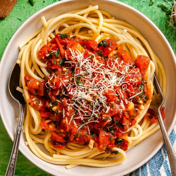 A plate of spaghetti topped with tomato sauce, chopped herbs, and grated cheese, with a fork and spoon on the sides.