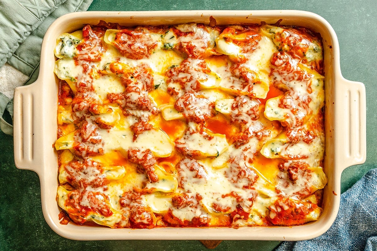 A rectangular baking dish filled with baked stuffed shells covered in tomato sauce and melted cheese.