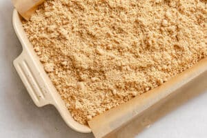 A rectangular baking dish lined with parchment paper, filled with an even layer of unbaked crumbly streusel topping.
