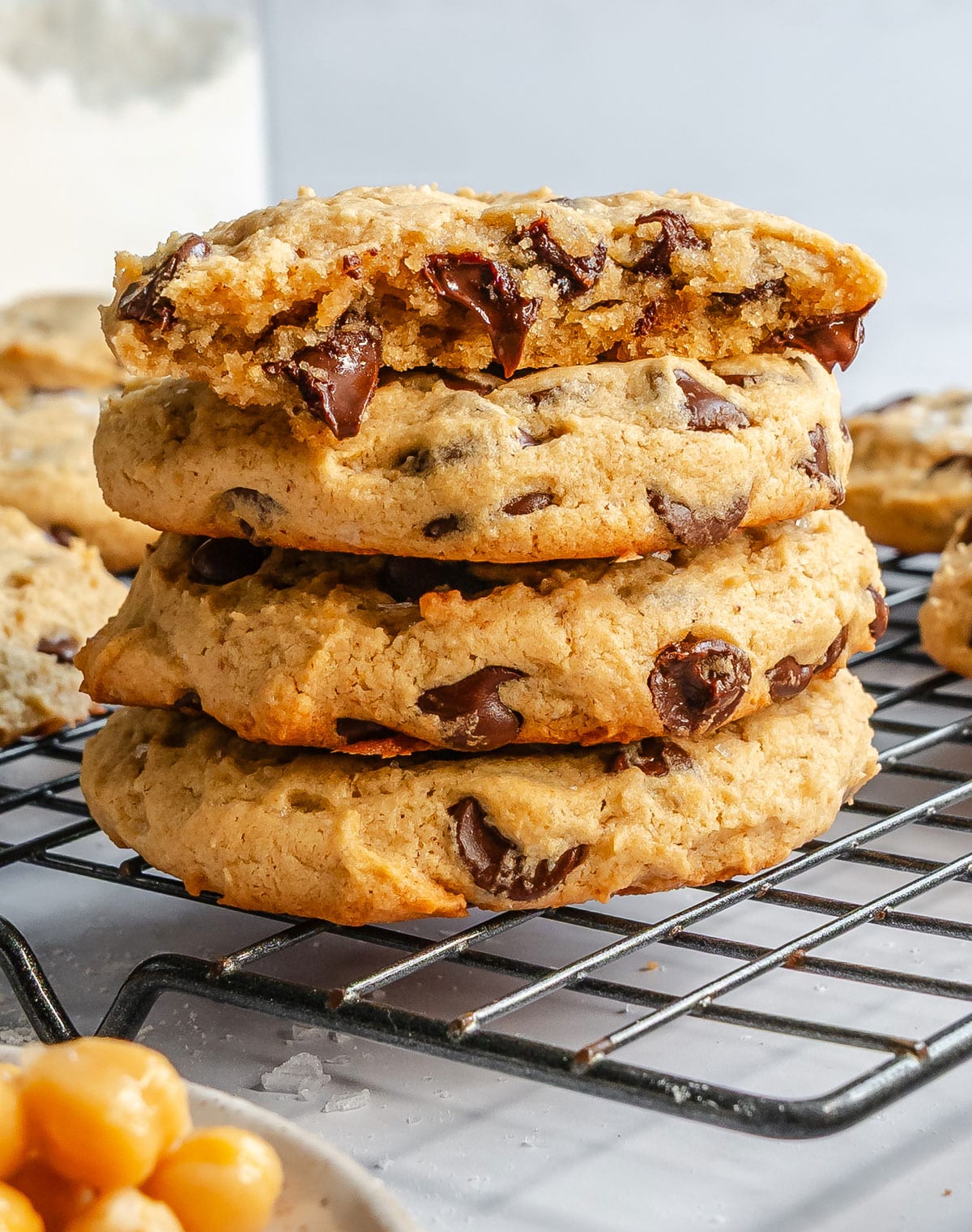 A stack of three chocolate chip chickpea cookies sits on a cooling rack, with a fourth cookie broken in half resting on top.