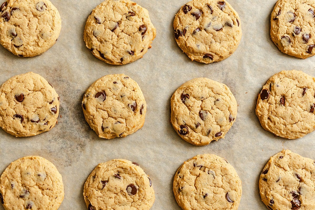 Twelve chocolate chip cookies arranged in rows on a sheet of parchment paper.