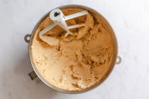 A mixing bowl with a paddle attachment contains creamed butter and sugar on a white surface.