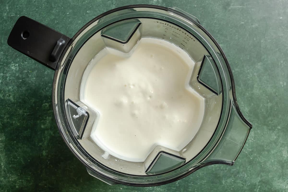 A top-down view of a blender containing a creamy white mixture on a green countertop.