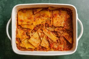 A casserole dish filled with layered pasta sheets and meat sauce, resembling an unbaked or deconstructed lasagna, on a green surface.