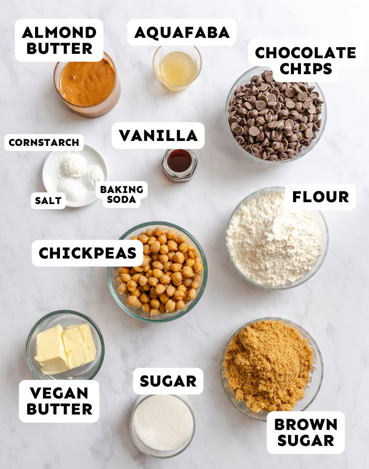 Various labeled baking ingredients, including almond butter, aquafaba, chocolate chips, vanilla, chickpeas, vegan butter, flour, sugar, brown sugar, cornstarch, salt, and baking soda.