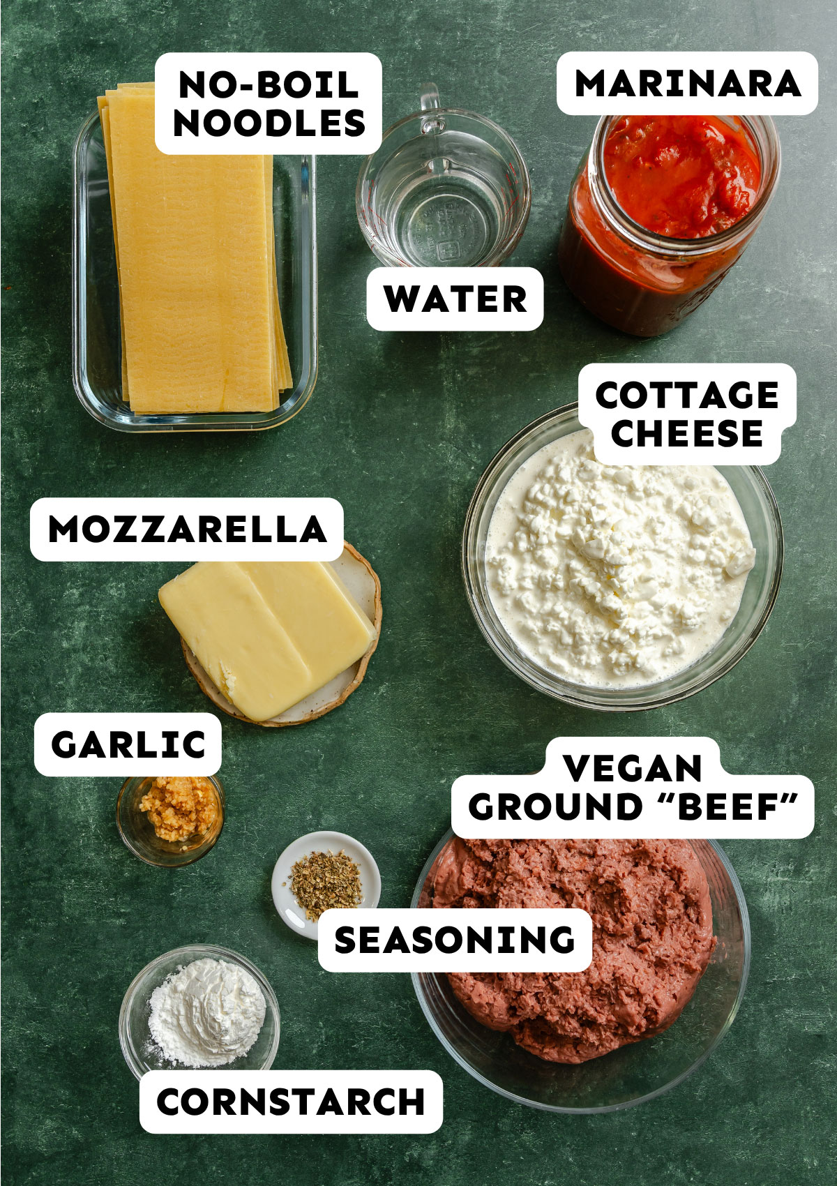 Flat lay of Lazy Lasagna Casserole ingredients labeled: no-boil noodles, marinara, water, cottage cheese, mozzarella, garlic, vegetarian ground beef, seasoning, and cornstarch for an easy dump and bake recipe on a green surface.
