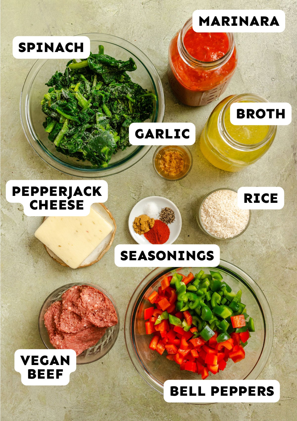 Top-down view of labeled ingredients for Unstuffed Pepper Casserole: spinach, pepperjack cheese, vegetarian vegan beef, bell peppers, seasonings, garlic, marinara sauce, broth, and rice—perfect for a dump and bake meal.
