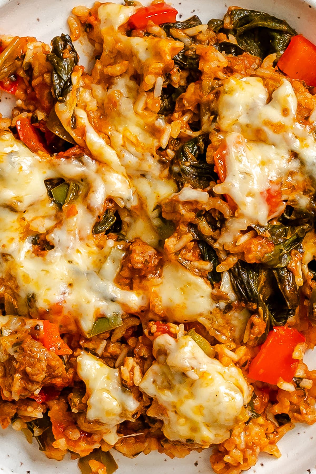A close-up of a baked rice dish with melted cheese, red bell peppers, spinach, and seasoned ground meat.