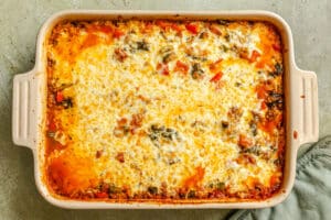 A baked casserole dish filled with a cheesy, golden-brown top and visible pieces of vegetables in a creamy, tomato-based sauce.