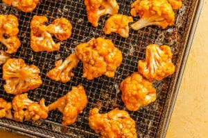 Buffalo sauce-coated cauliflower florets arranged on a wire rack over a baking sheet, ready for cooking.