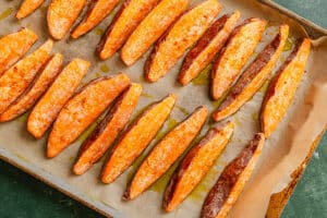 Potato wedges arranged on a parchment-lined baking sheet, lightly coated with oil and baked to a golden brown.