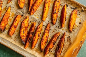 Baked potato wedges arranged on a parchment-lined baking sheet, showing a crispy, golden-brown exterior.