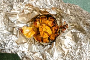 A head of roasted garlic sits on crumpled aluminum foil, with cloves exposed and caramelized.