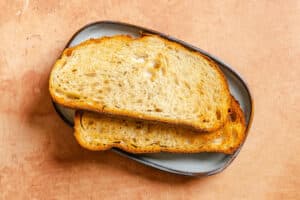 Two slices of toasted bread are stacked on a small gray plate placed on a light brown surface.